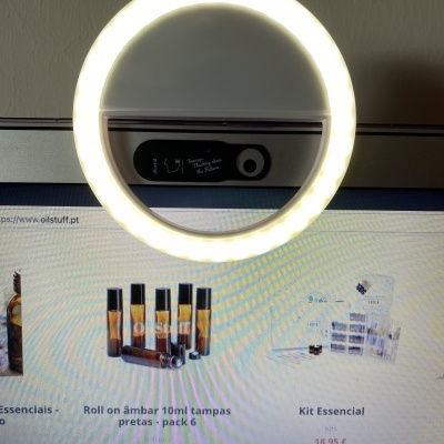 Anel de luz LED circular branco sobre monitor a exibir produtos aromáticos com frascos âmbar e kits essenciais