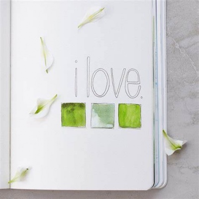 Página branca de caderno com texto 'i love.' e três quadrados verdes, rodeada por pétalas de flores brancas sobre superfície cinza