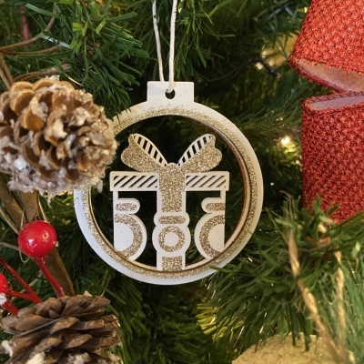 Enfeite de Natal em madeira branca e dourada pendurado numa árvore verde com pinhas e fitas vermelhas