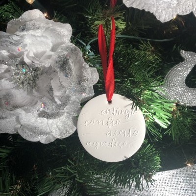 Ornamento redondo branco gravado pendurado numa árvore de Natal com flores brancas e luzes