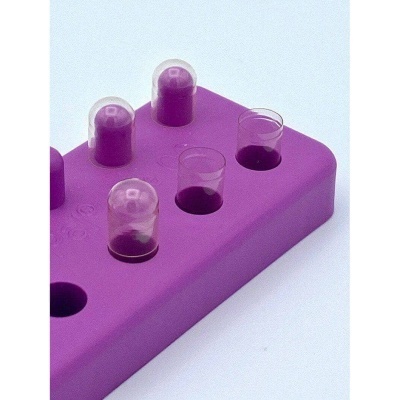 Peça de silicone roxa com cilindros transparentes e líquidos roxos.