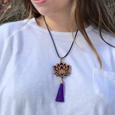 Colar com pendente de flor de lótus em madeira e franjas roxas sobre t-shirt branca