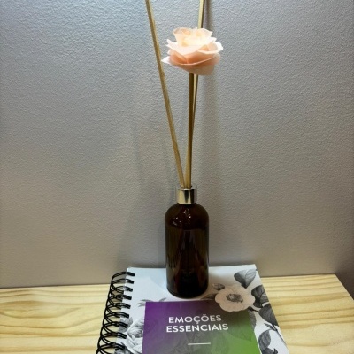 Frasco castanho com varetas e flor sobre caderno floral e folheto