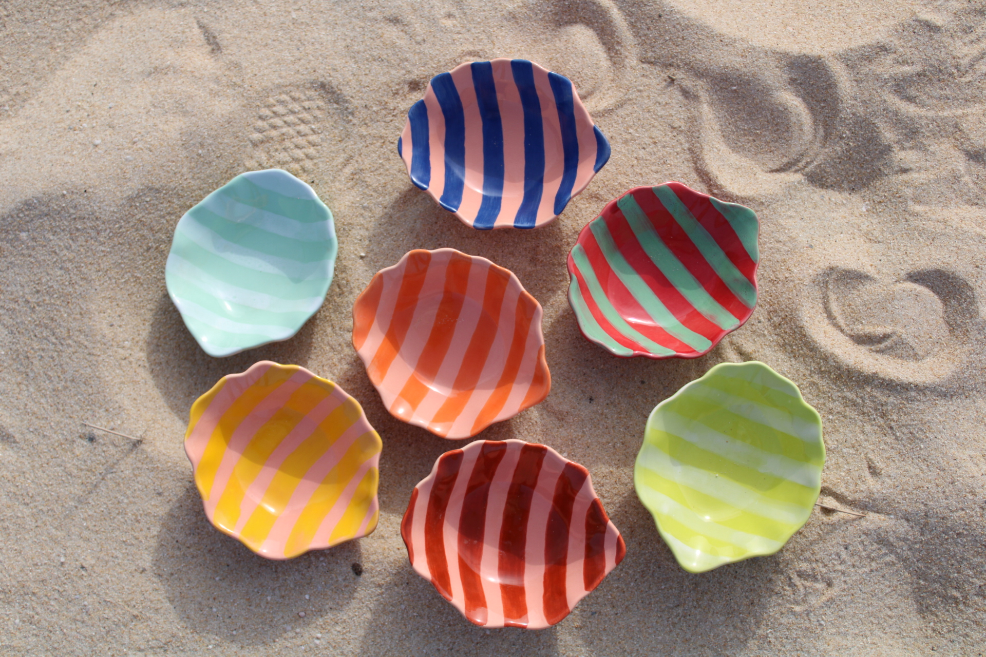Tigelinha Mar Pequenos pratos cerâmicos coloridos com riscas sobre areia