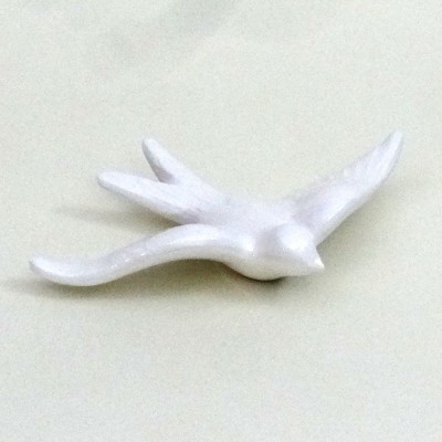 Escultura branca em forma de pássaro em voo sobre superfície clara