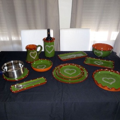 Conjunto de loiça verde com bordas alaranjadas e corações brancos numa mesa preta