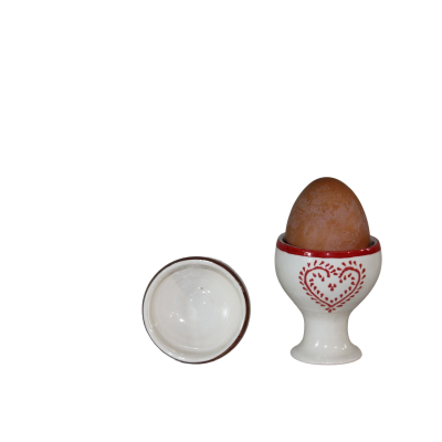 Ovo castanho numa colher de ovos branca com padrão de coração vermelho e outra colher branca de lado