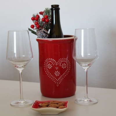 Garrafa numa cubeta vermelha com decoração de coração, dois copos de vidro e prato com amêndoas