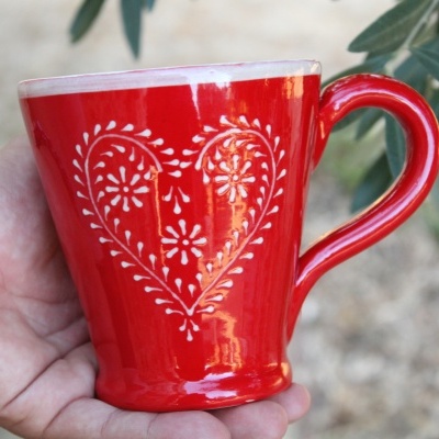 Caneca cerâmica vermelha com padrão de coração branco decorativo.