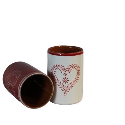 Dois copos de cerâmica com padrão de coração, um creme e outro vermelho