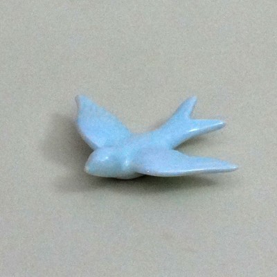 Figura azul claro de pássaro em cerâmica sobre superfície bege