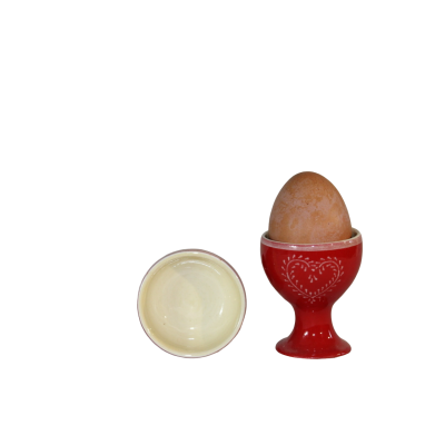 Ovo castanho num suporte para ovos vermelho em cerâmica com padrão branco e taça branca ao lado.