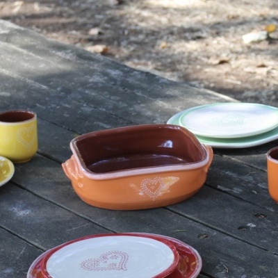 Conjunto de pratos e canecas em cerâmica colorida com decoração de corações sobre mesa de madeira rústica