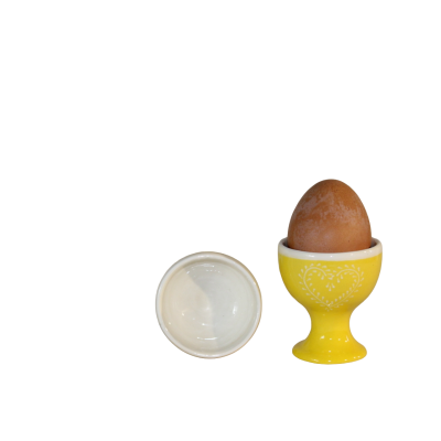 Ovo castanho em suporte amarelo decorado com padrão de coração branco e tampa branca ao lado