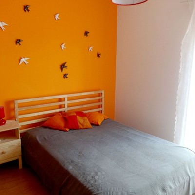 Quarto com cama cinza, almofadas laranja, parede laranja e decoração de pássaros