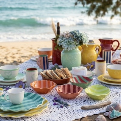 Mesa posta com louça colorida e flores, à beira da praia