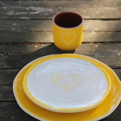 Copos e pratos com padrão de coração amarelo e branco sobre mesa de madeira