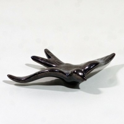 Estatueta preta de pássaro com asas estendidas sobre superfície branca