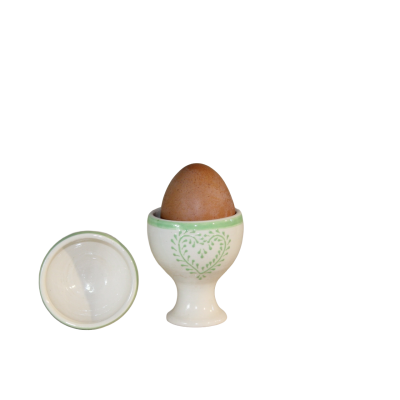 Ovo castanho em suporte de ovo cerâmico branco com detalhes verdes e tampa ao lado.