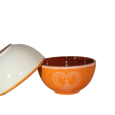 Duas tigelas de cerâmica, uma branca virada para baixo e outra laranja com padrão de coração branco.