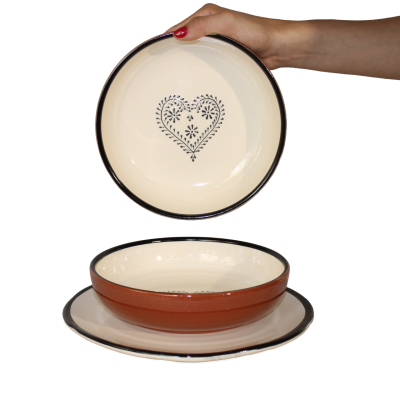 Conjunto de pratos de cerâmica creme e castanho com decoração de coração e borda preta, mão a segurar o prato superior