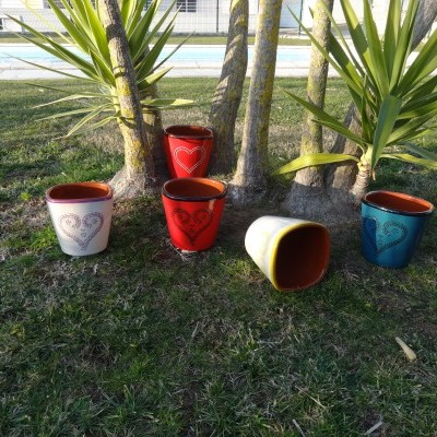 Cinco vasos de cerâmica coloridos com padrão de corações na relva junto a árvores