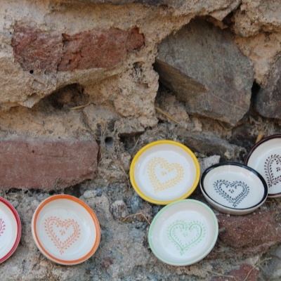 Tigelas cerâmicas coloridas com decoração de coração junto a uma parede rústica de pedra e tijolo.
