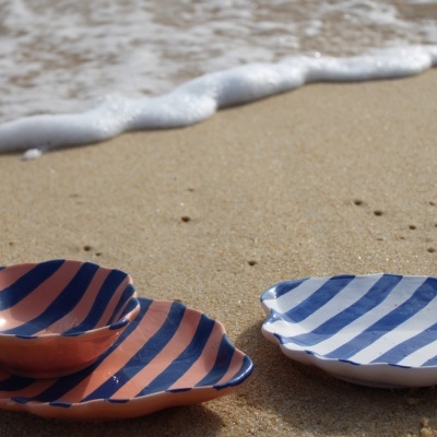 Dois pratos decorativos em forma de concha na areia com ondas de mar ao fundo