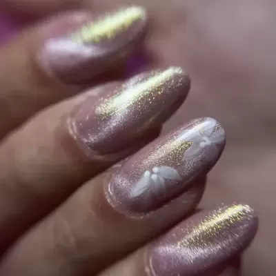 Unhas rosa perolado com brilho dourado e flores brancas decorativas.