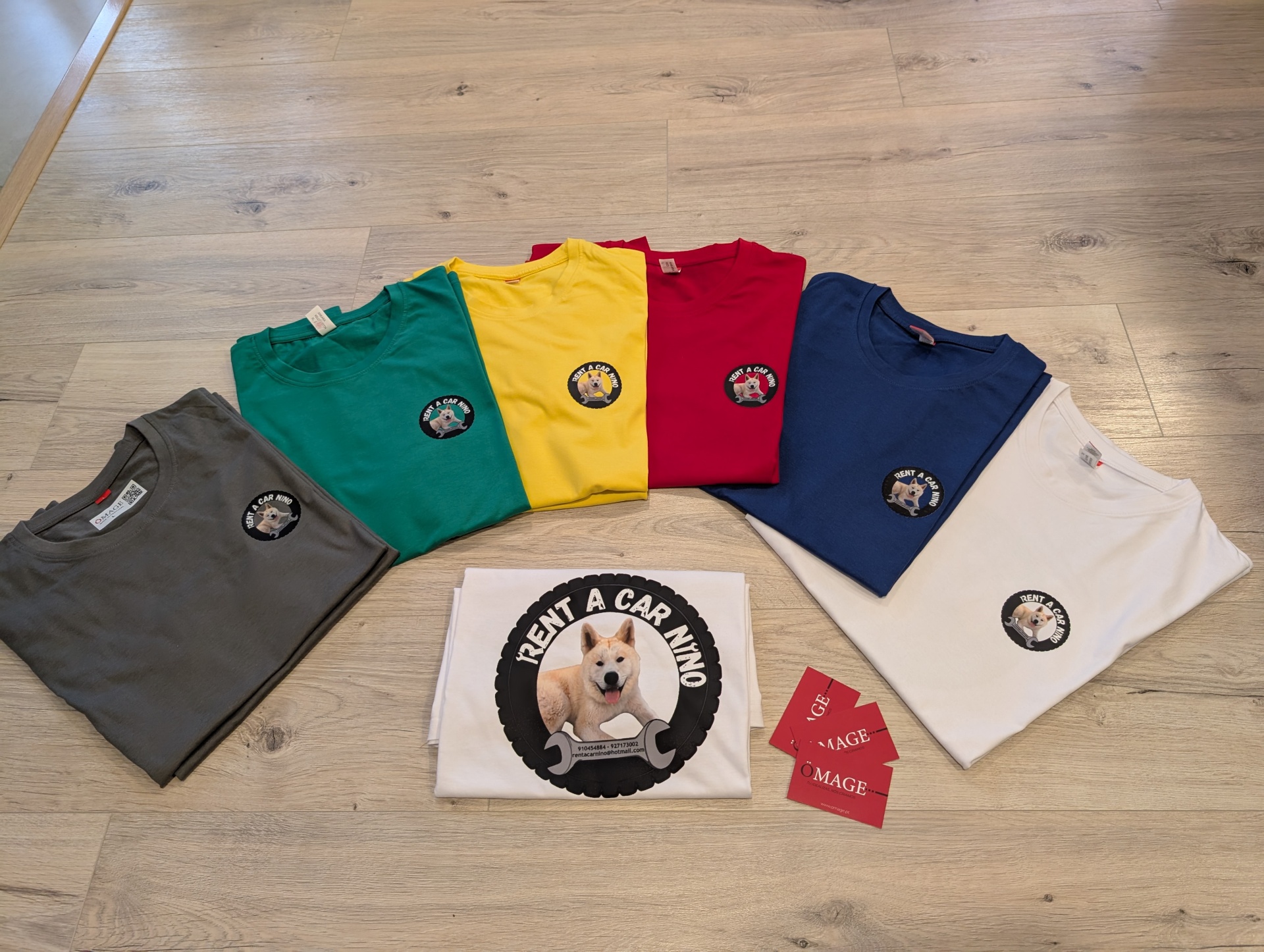 Seis t-shirts coloridas com logotipo de cão e etiquetas 'IMAGE' sobre chão de madeira clara