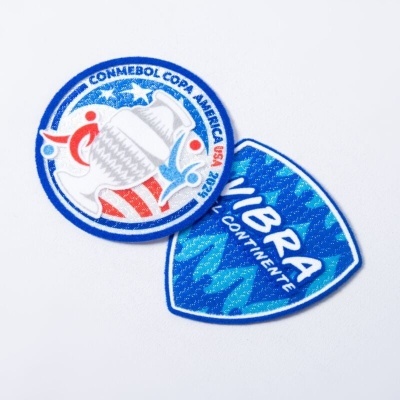 Dois patches bordados, um redondo da Copa América e um em forma de escudo azul com texto VIBRA CONTINENTE.