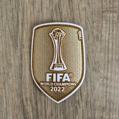 Emblema de patch FIFA World Champions 2022 em escudo dourado sobre madeira