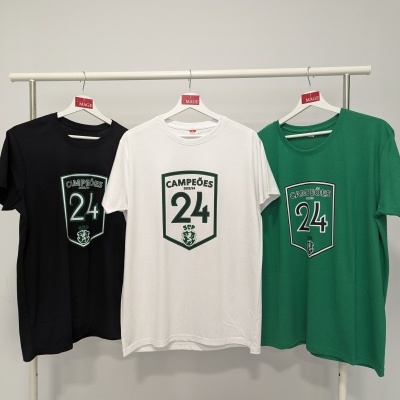 Três t-shirts em preto, branco e verde com texto CAMPEÕES 24 em escudo penduradas num cabideiro branco