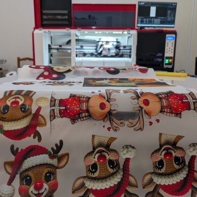 Tecido branco com estampado natalício de renas em malha à frente de impressora a cores.