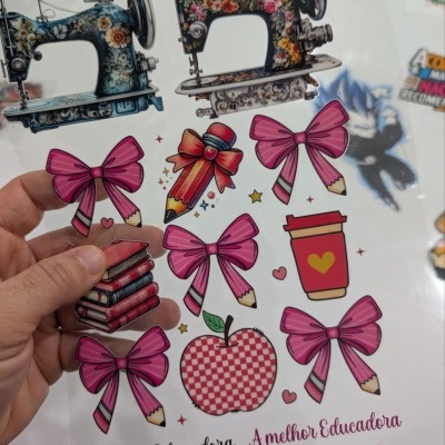 Autocolantes variados com máquinas de costura, laços, livros, maçã e texto 'A melhor Educadora' em folhas transparentes
