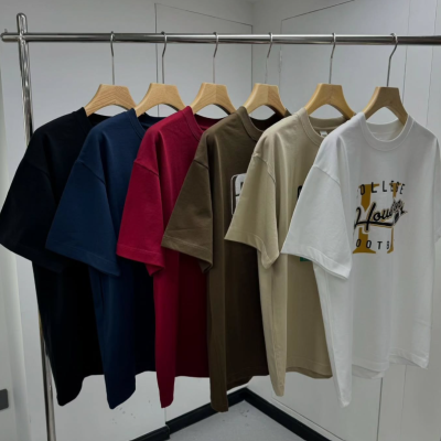 Seis t-shirts coloridas penduradas num varão com cabides de madeira