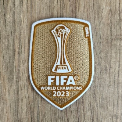 Emblema FIFA World Champions 2023 em tons dourado e branco sobre madeira.