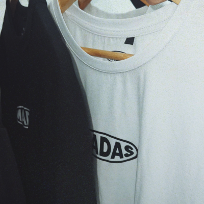 Duas t-shirts, preta e branca, penduradas em cabides de madeira numa parede clara