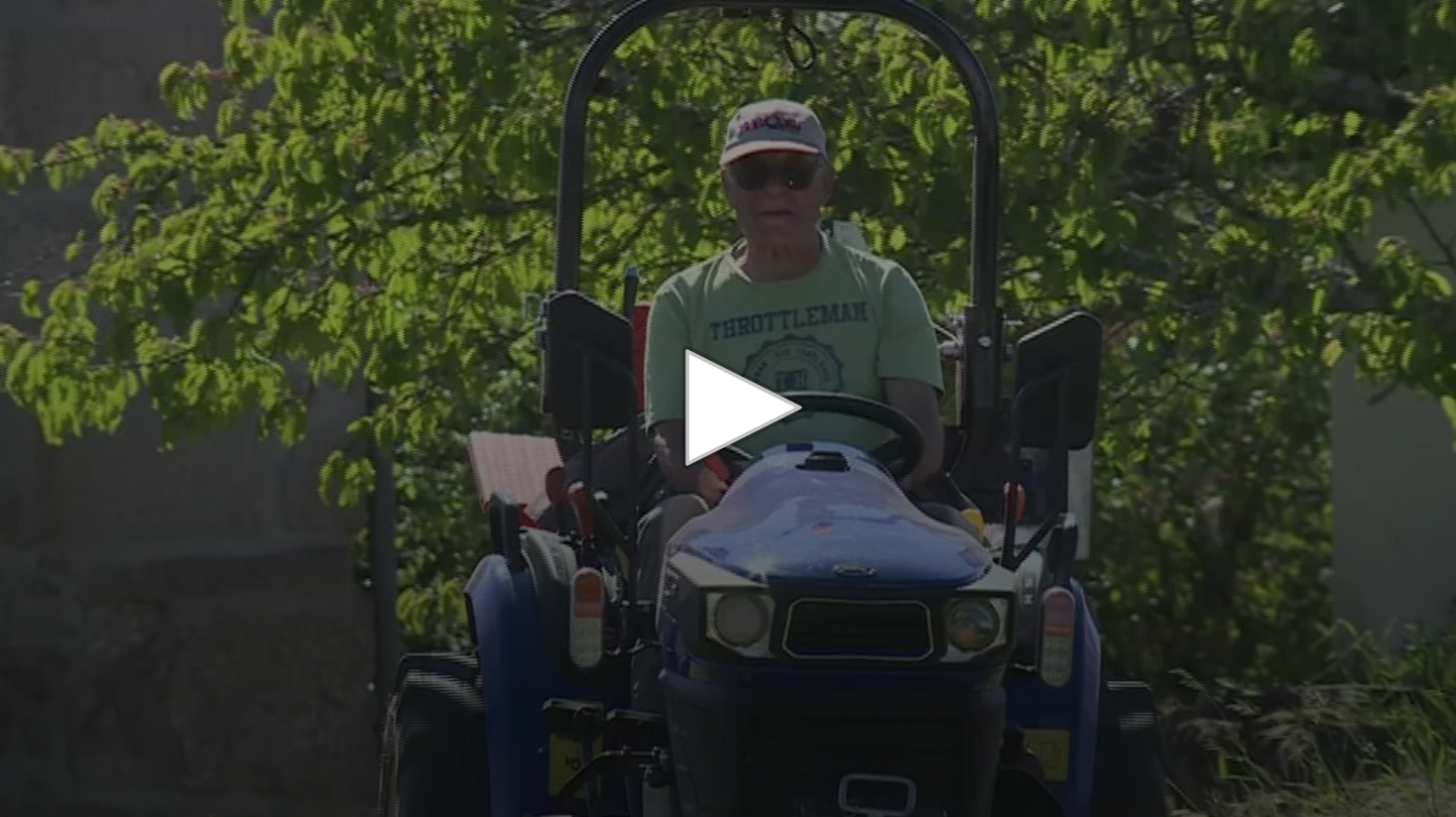 Homem no trator azul com t-shirt verde claro e chapéu preto ao ar livre