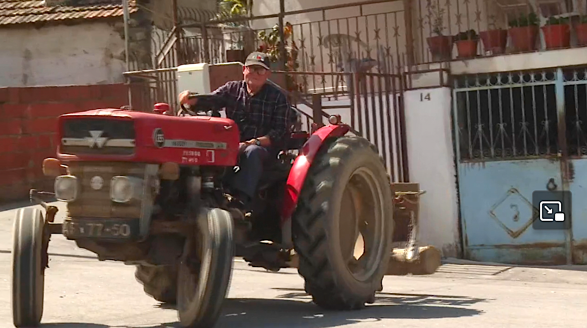 Trator vermelho Massey Ferguson 135 numa rua com casas ao fundo