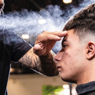 Pessoa a receber spray transparente no cabelo com braço tatuado visível