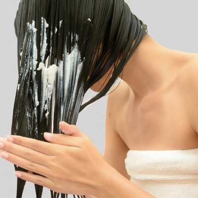 Pessoa aplicando produto no cabelo com toalha branca em fundo cinza