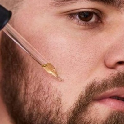 Homem aplicando líquido dourado na bochecha com conta-gotas