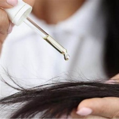 Pessoa a aplicar líquido com conta-gotas em cabelo preto