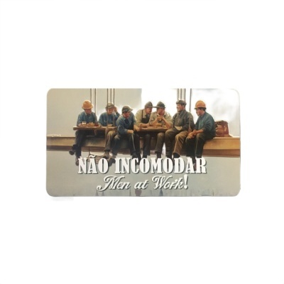 Cartaz com operários numa viga e texto 'NÃO INCOMODAR Men at Work!'.