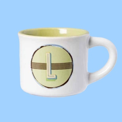 Caneca branca com interior amarelo e decoração com letra L amarilla num círculo.