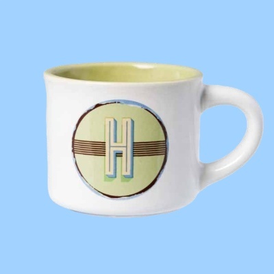 Caneca branca em cerâmica com interior amarelo claro e letra H azul no círculo verde
