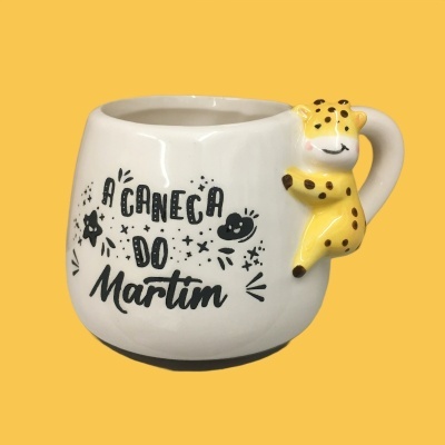Caneca branca com texto e um animal amarelo agarrado à asa.