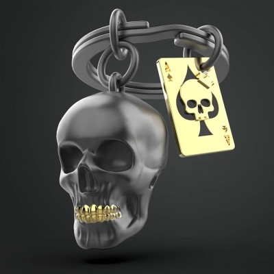 Chaveiro metálico com caveira cinzenta e cartão dourado com ás de espadas.