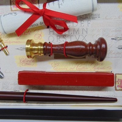Conjunto de escrita para carimbo em madeira e metal dourado com tampa vermelha e caneta de madeira castanha, numa caixa decorativa.